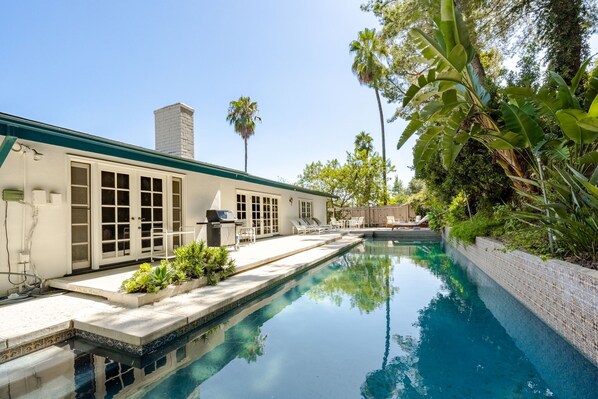 A swimming pool with a tiled edge, a covered patio with lounge chairs, and a white building with large windows and a chimney. - 4BR w/Heated Pool/Spa and Game Room (Los Angeles)