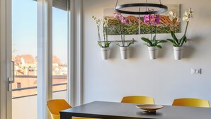 Comedor con mesa y sillas, un arreglo colgante de orquídeas y vista a la ciudad a través de ventanas amplias.
