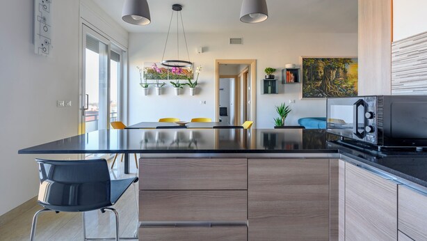 Una cocina moderna con una isla central, iluminación colgante y vistas al comedor.