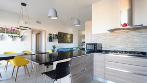 Una cocina moderna con una isla central, iluminación colgante y un comedor con sillas amarillas.