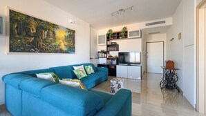 Una sala moderna con un sofá verde azulado, un cuadro grande, una estantería, un televisor y una pequeña mesa con una planta.