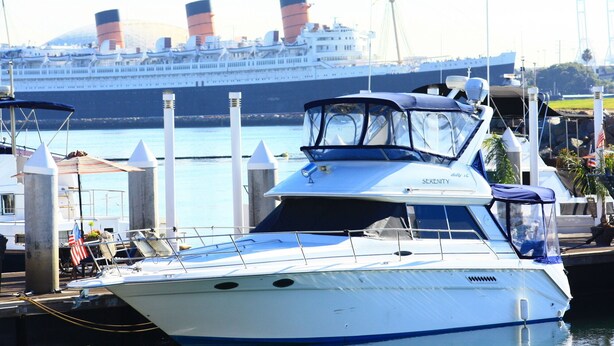 A boat docked at a marina with a large cruise ship in the background.