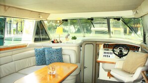 A boat interior with a cushioned seating area, a wooden table, and a control panel with gauges.