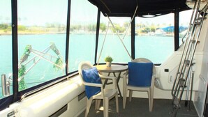 A small, enclosed deck area with a table and two chairs, overlooking a body of water.