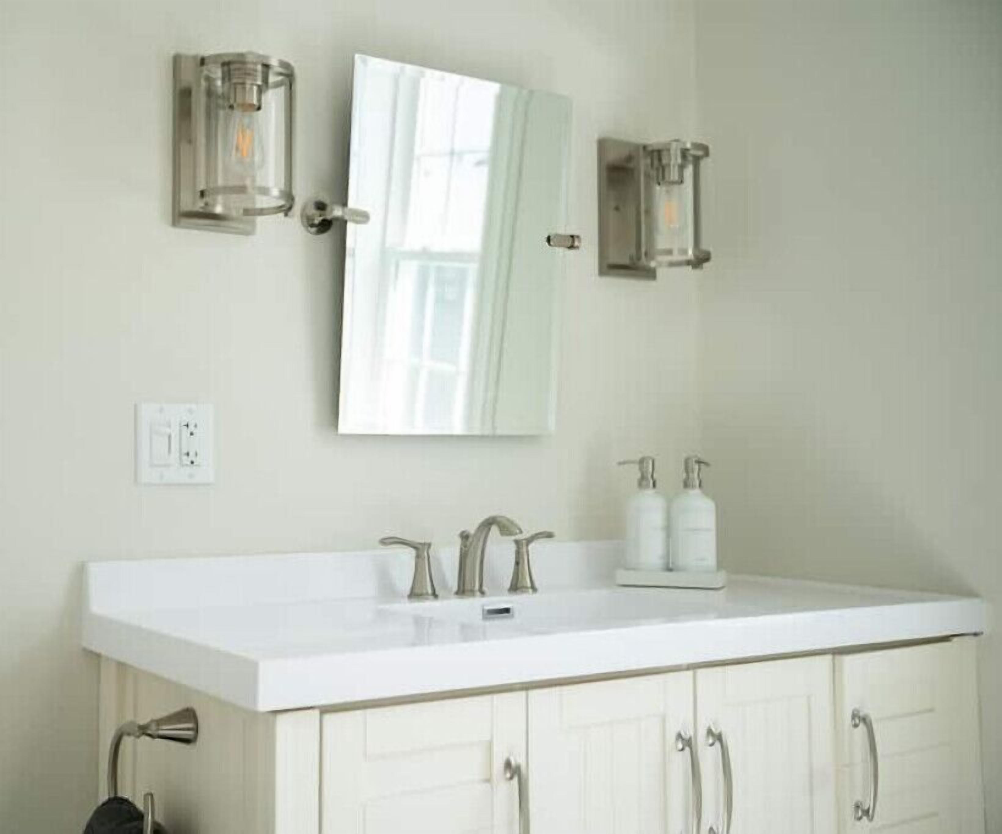 Un baño con tocador blanco, un espejo grande y dos apliques de pared.