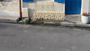Un edificio con puerta y contraventanas azules, una ventana pequeña con cortinas blancas y el número '49' sobre la puerta.