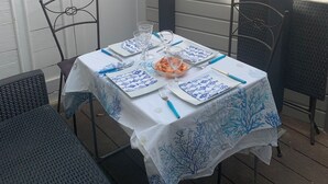 Un patio con una mesa dispuesta para comer, rodeado de sillas de metal y una puerta blanca.