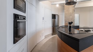 Cozinha moderna com eletrodomésticos embutidos, uma ilha central e uma área de refeições com uma cadeira.