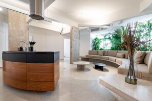 A modern living room with a curved wooden cabinet, a round coffee table, a beige sofa, and a large window with greenery. - Wonderful in Copacabana 2 Bedrooms Nsc501b (Rio de Janeiro)