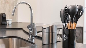 Cozinha com pia de aço inoxidável, torneira moderna e suporte para utensílios com colheres de madeira.