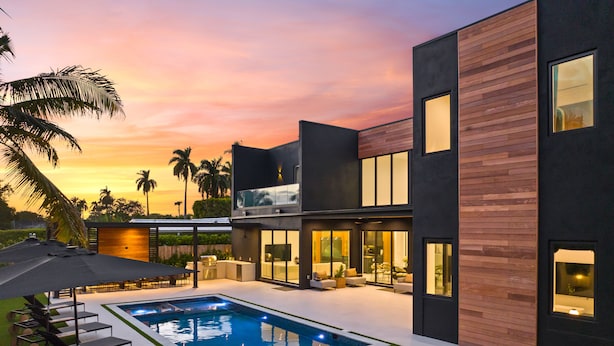 Een moderne villa met een zwembad, terrasmeubilair en uitzicht op palmbomen bij zonsondergang.
