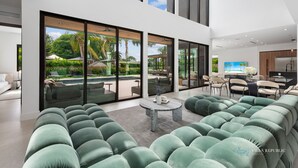Een moderne woonkamer met een ruime hoekbank, een marmeren salontafel en uitzicht op een zwembad en terras via grote glazen deuren.
