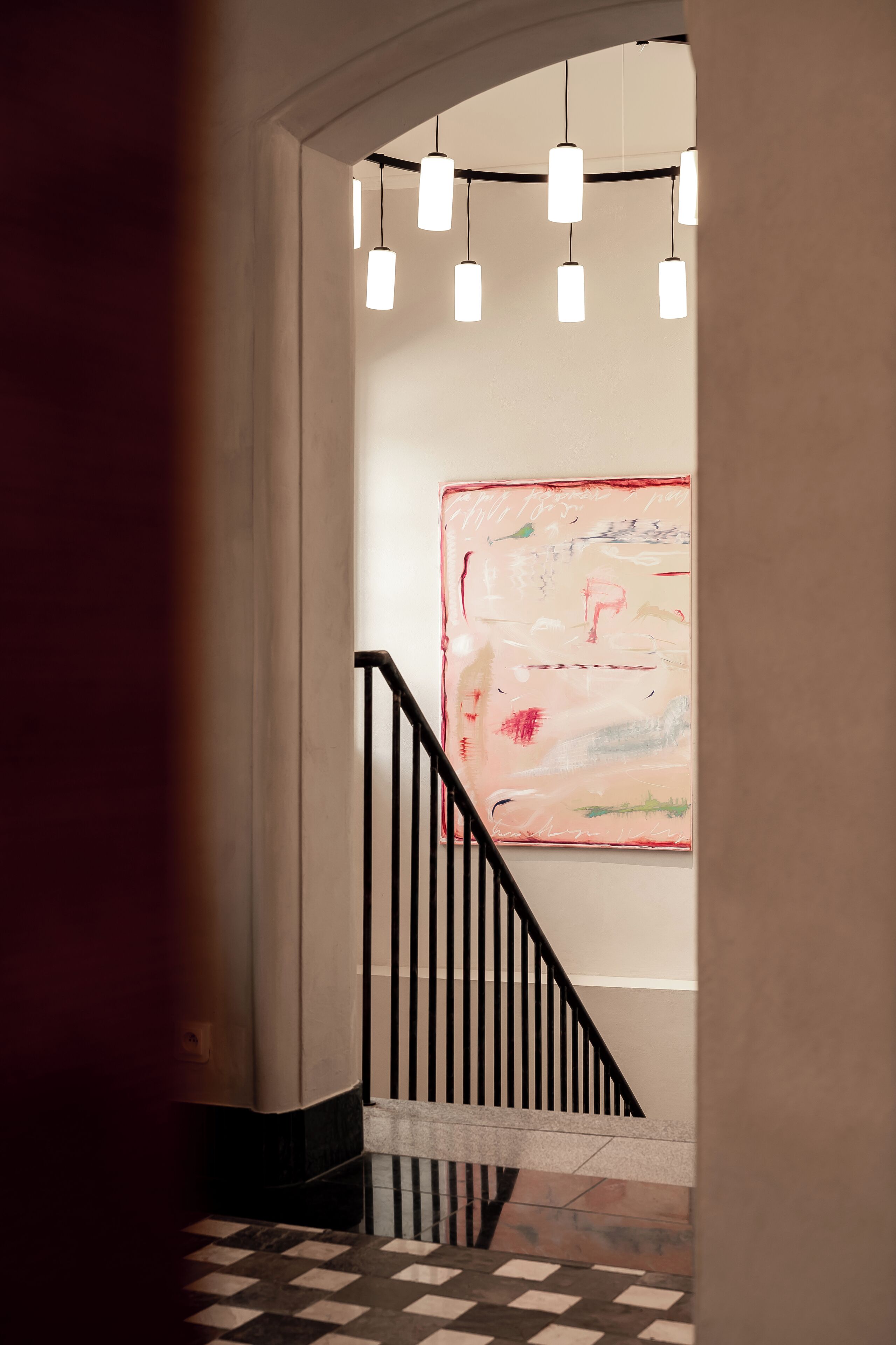A hallway with a black railing, a checkered floor, and hanging pendant lights.