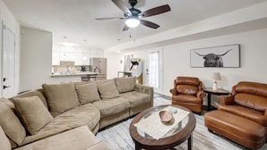 A modern living room with a beige sectional sofa, leather armchairs, and a coffee table. A ceiling fan and a bull-themed artwork are visible. - Game-Day Getaway NEW Stadium View Walk to ATT or Rangers (Arlington)