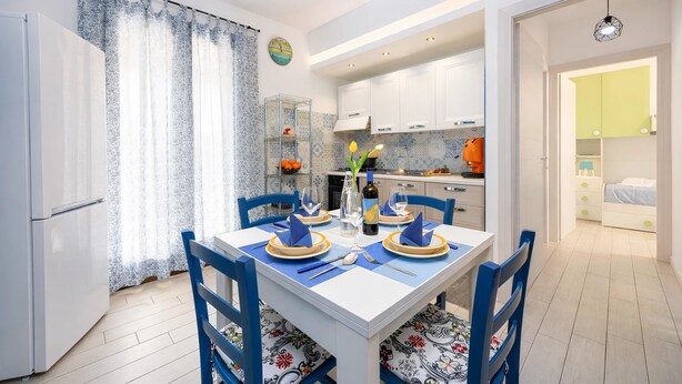 A dining area with a white table, blue chairs, and a patterned table runner. - Dolceluna Apartment - San Vito Lo Capo (TP) (San Vito Lo Capo)