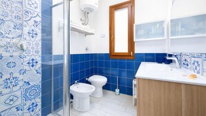 A bathroom with blue and white tiles, a white sink, a wooden cabinet, and a shower area. - Dolceluna Apartment - San Vito Lo Capo (TP) (San Vito Lo Capo)