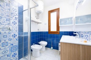 Un baño con azulejos azules y blancos, un lavabo blanco, un armario de madera y una zona de ducha.