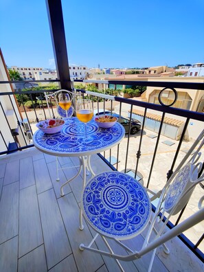 Un balcón con una mesa y sillas, un cuenco de aperitivos y una copa de bebida.