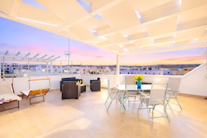 A rooftop terrace with a dining area, seating, and a view of the cityscape.