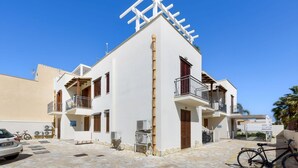 A two-story building with balconies, a car parked in front, and a bicycle. - Dolceluna Apartment - San Vito Lo Capo (TP) (San Vito Lo Capo)