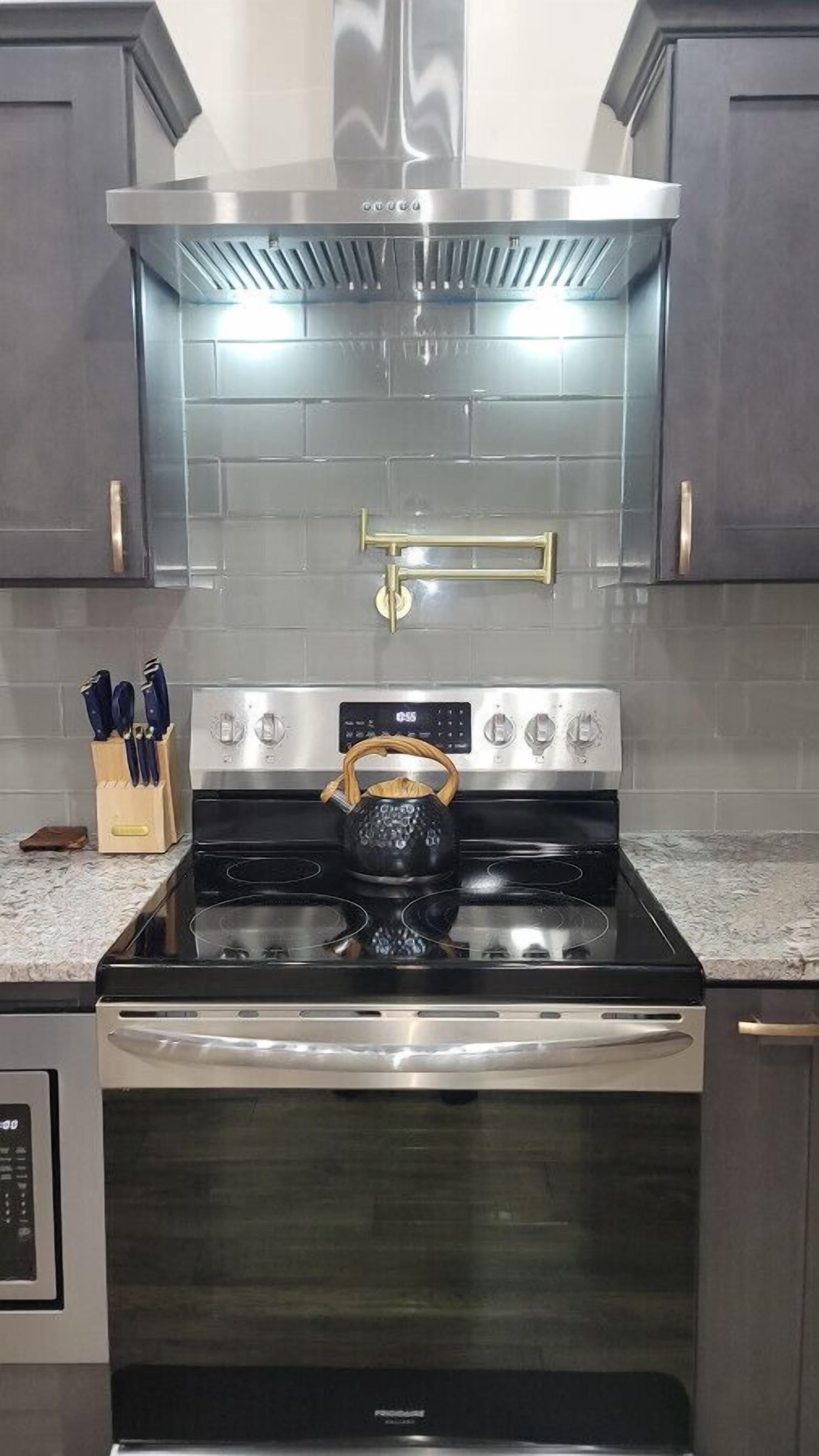 Una cocina con extractor de acero inoxidable, una estufa negra con un hervidor y un microondas.