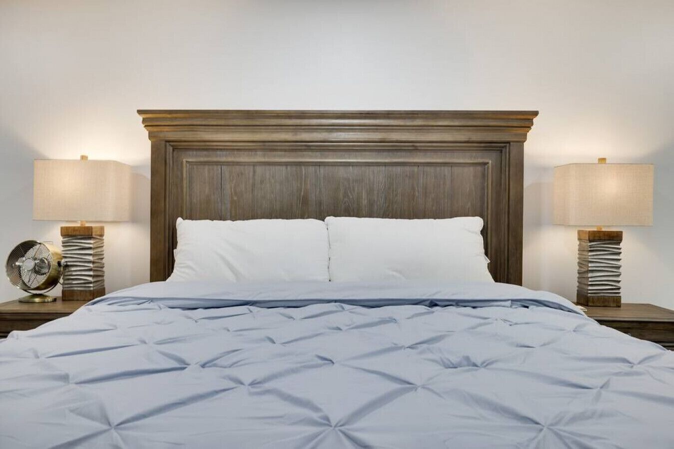 Una cama bien hecha con cabecera de madera, dos lámparas de noche y una pila de libros en cada mesita.