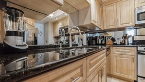 Una cocina moderna con armarios de madera, encimera de granito, una licuadora, una cafetera y electrodomésticos de acero inoxidable.
