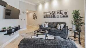 Una sala de estar moderna con un sofá gris, un televisor de pantalla plana, una mesa de centro y una obra de arte decorativa en la pared.