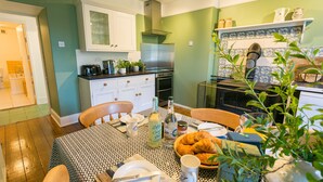 Un comedor con una mesa preparada para dos personas, una cafetera y una cesta de cruasanes.