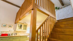 Un escalier en bois menant à un deuxième étage, une cuisine avec des meubles verts et une cheminée blanche ornée de livres.