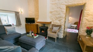 Un salon chaleureux avec un mur en pierre, une cheminée, un canapé, un téléviseur et un coin repas comprenant une table et des chaises.
