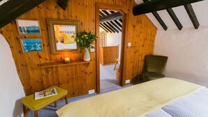 Une chambre confortable aux murs en bois, avec un lit, une petite table sur laquelle repose un magazine et un fauteuil vert.