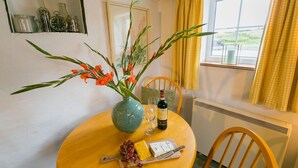Une table à manger ornée d’un vase de fleurs, d’une bouteille de vin et d’une assiette de fromage et de raisins.