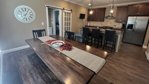 Une cuisine moderne avec des meubles de couleur bois foncé, un réfrigérateur en acier inoxydable et un coin repas comprenant une table et des chaises en bois.