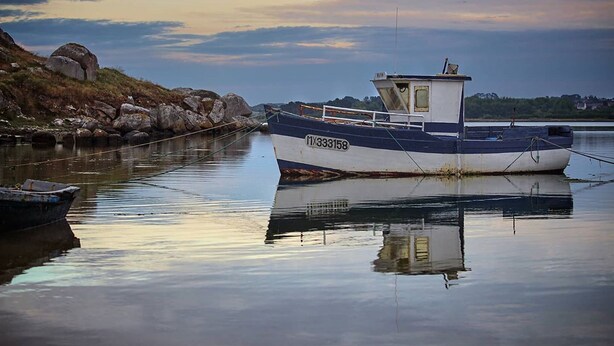 Un bateau était amarré dans un port tranquille, bordé d’une côte rocheuse, sous un ciel dégagé.