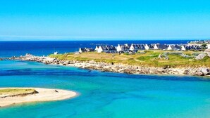 Une zone côtière caractérisée par des eaux turquoise et limpides, une plage de sable et des maisons blanches aux toits coniques.