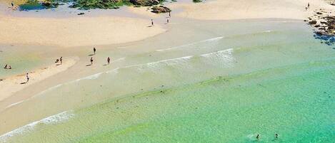 An aerial view of a beach with clear turquoise waters, rocky areas, and people engaging in water activities.