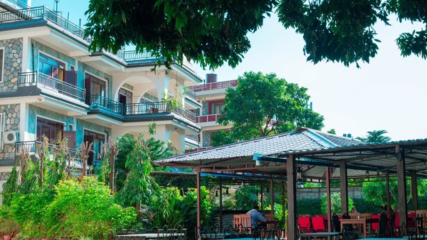 A multi-story building with balconies, a covered outdoor seating area with tables and chairs, and lush greenery. - Taj Residency Pokhara (Pokhara)