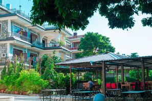 A multi-story building with balconies, a covered outdoor seating area with tables and chairs, and lush greenery. - Taj Residency Pokhara (Pokhara)