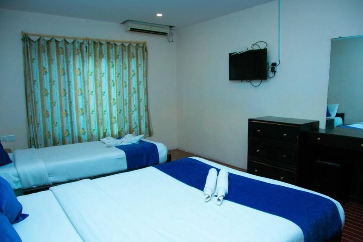 A hotel room with two beds, a flat-screen TV, a dresser, and a window with curtains.