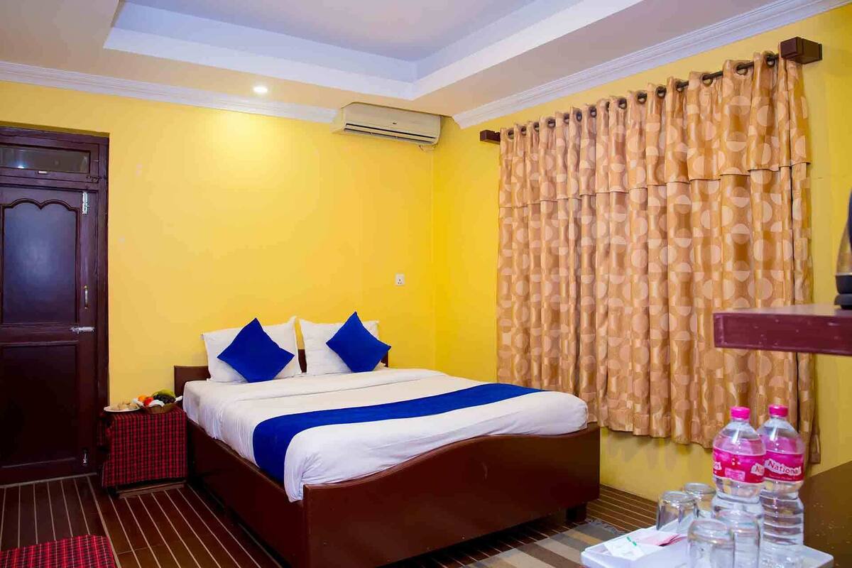 A hotel room with a bed, a table with a red checkered tablecloth, a water dispenser, and a bottle of water.