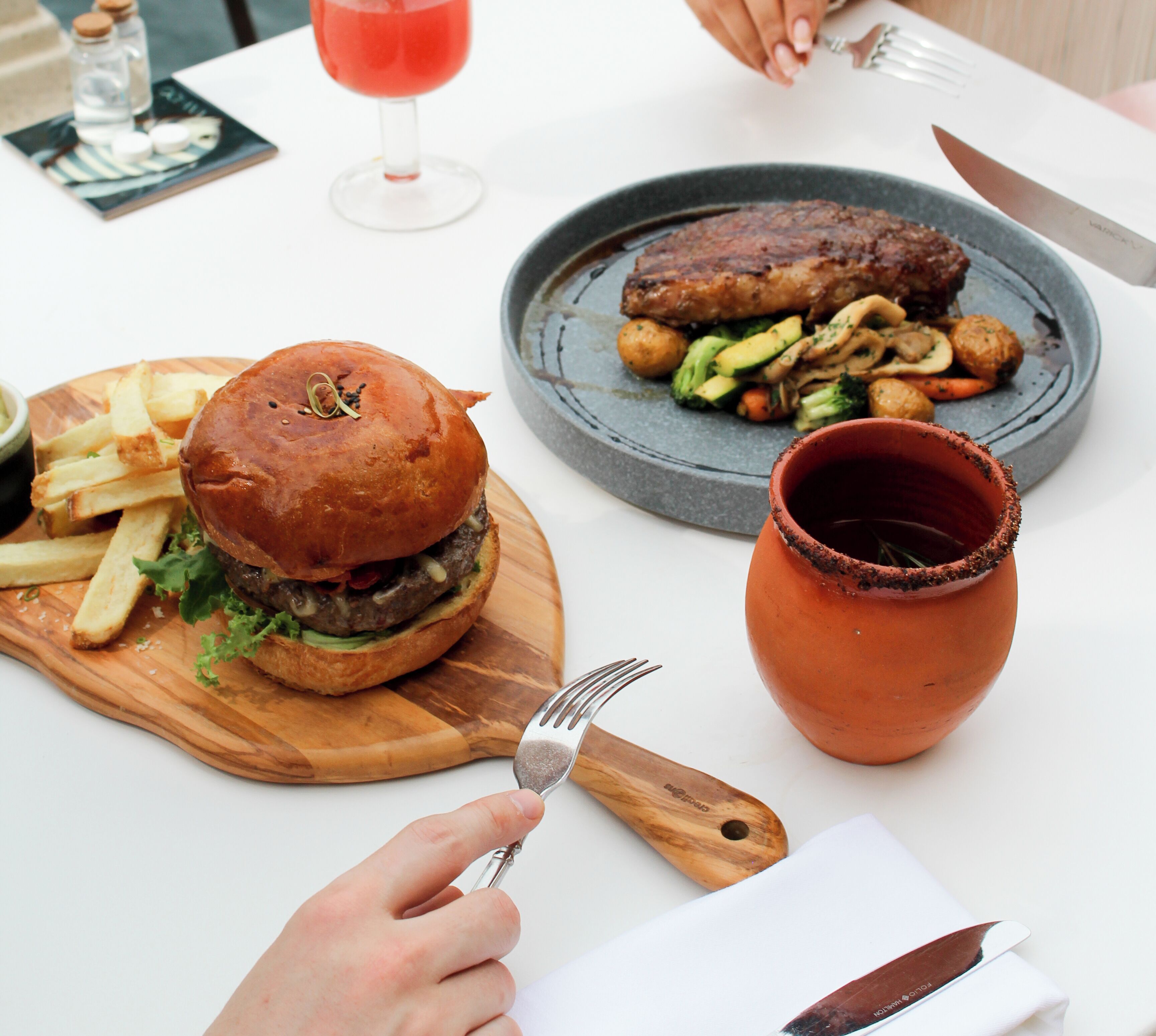 Eine Mahlzeit mit einem Burger, Pommes und einem Steakteller mit Gemüse.