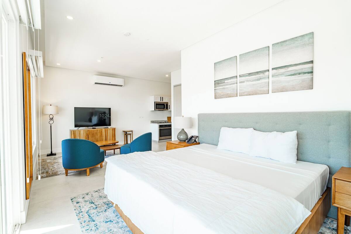 A modern hotel room with a large bed, a TV, a desk, and a chair.