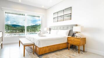 A bedroom with a large window, a bed, a bedside table, and a nightstand.