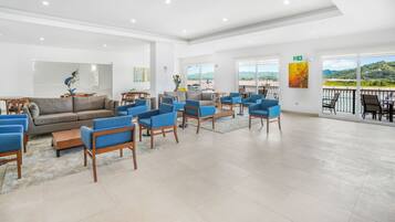 A spacious lobby with a grey sofa, blue armchairs, and a wooden coffee table. Large windows offer a view of the outdoors.