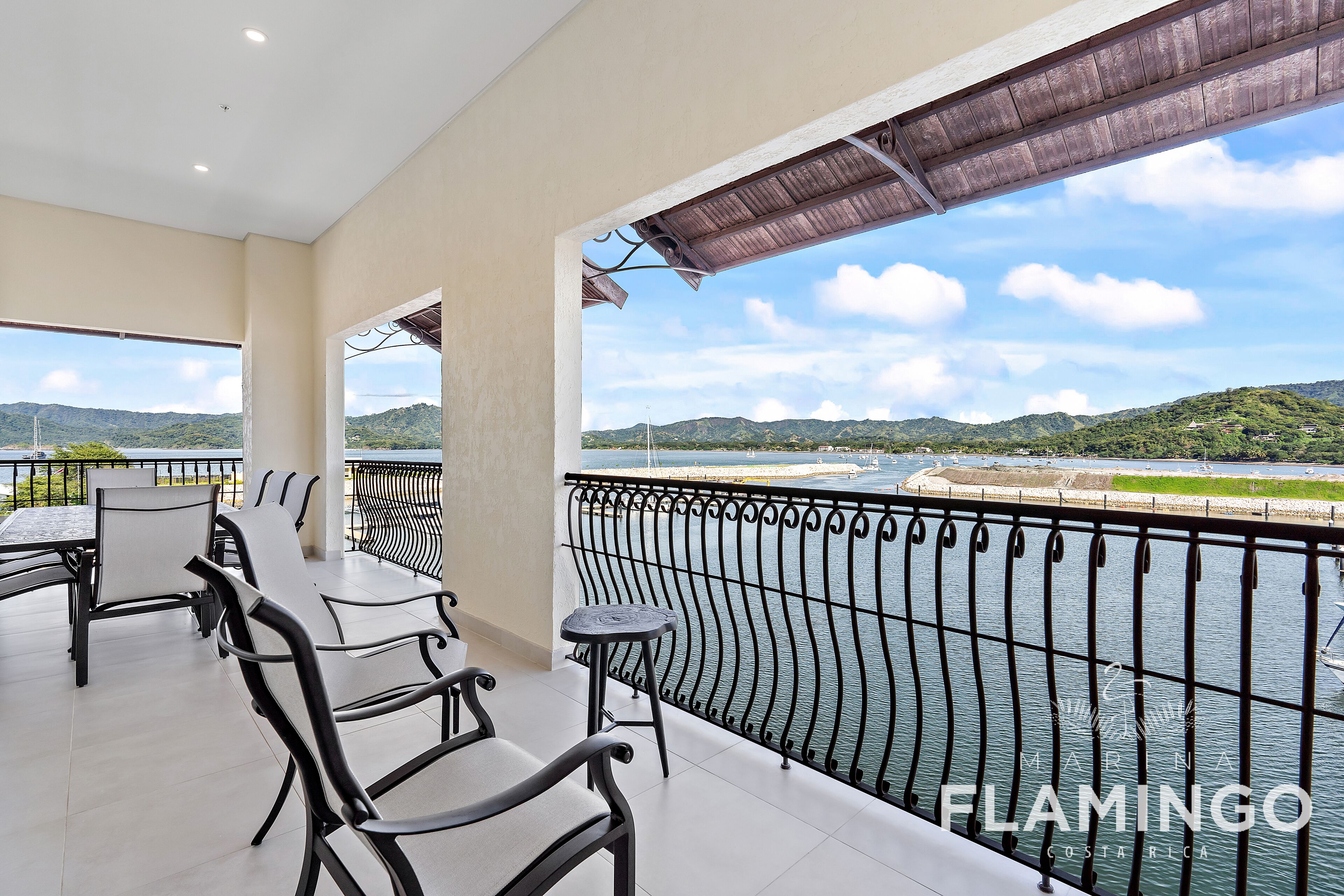 A balcony with outdoor seating, a view of a river, and a mountainous landscape.