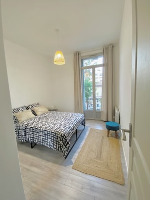 A bedroom with a bed, a window, a door, and a small stool.