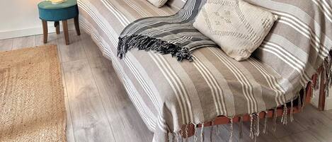 Una habitación con pared de ladrillo, un sofá con ropa de cama a rayas, un reloj con números romanos y una mesita con una lámpara.
