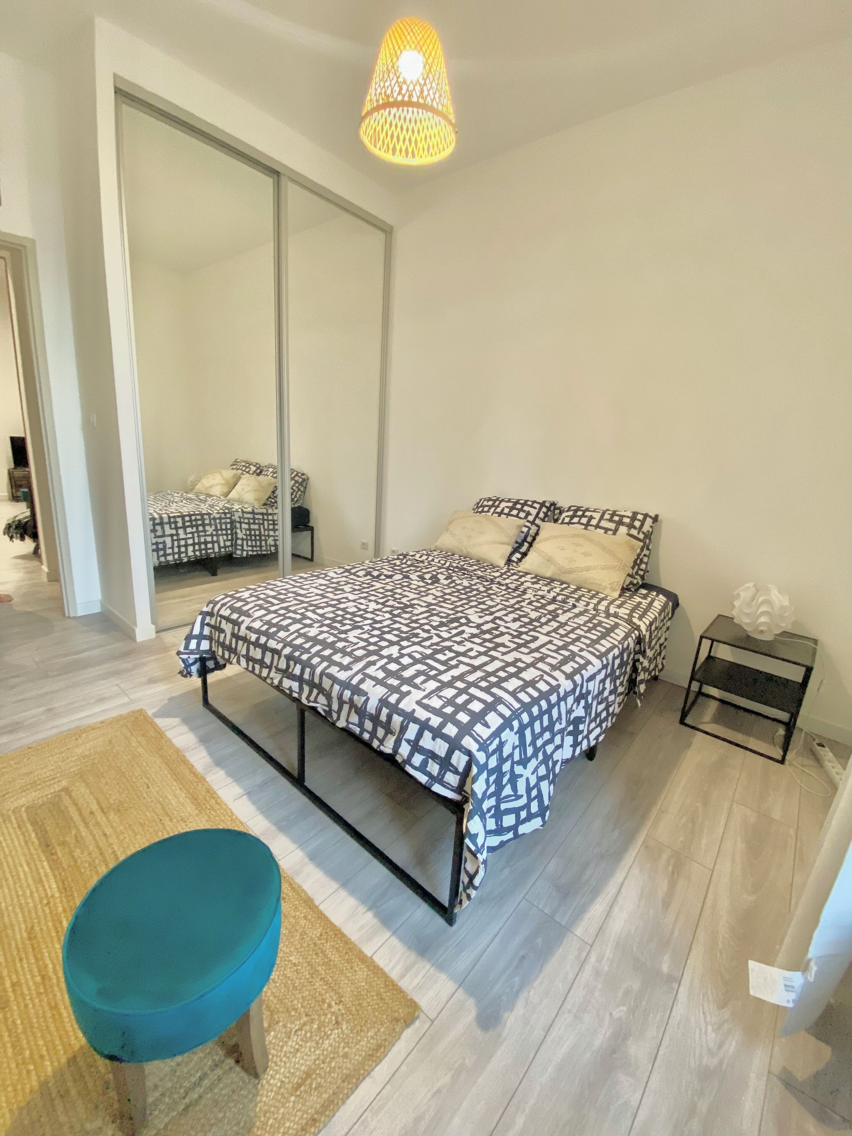 Ein Schlafzimmer mit einem Bett, einem kleinen Tisch, einem Sessel, einem Spiegel und einer Pendelleuchte.