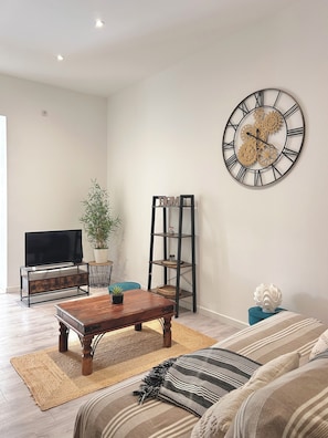 A living room with a wooden coffee table, a television on a stand, a bookshelf, a decorative clock, and a sofa.